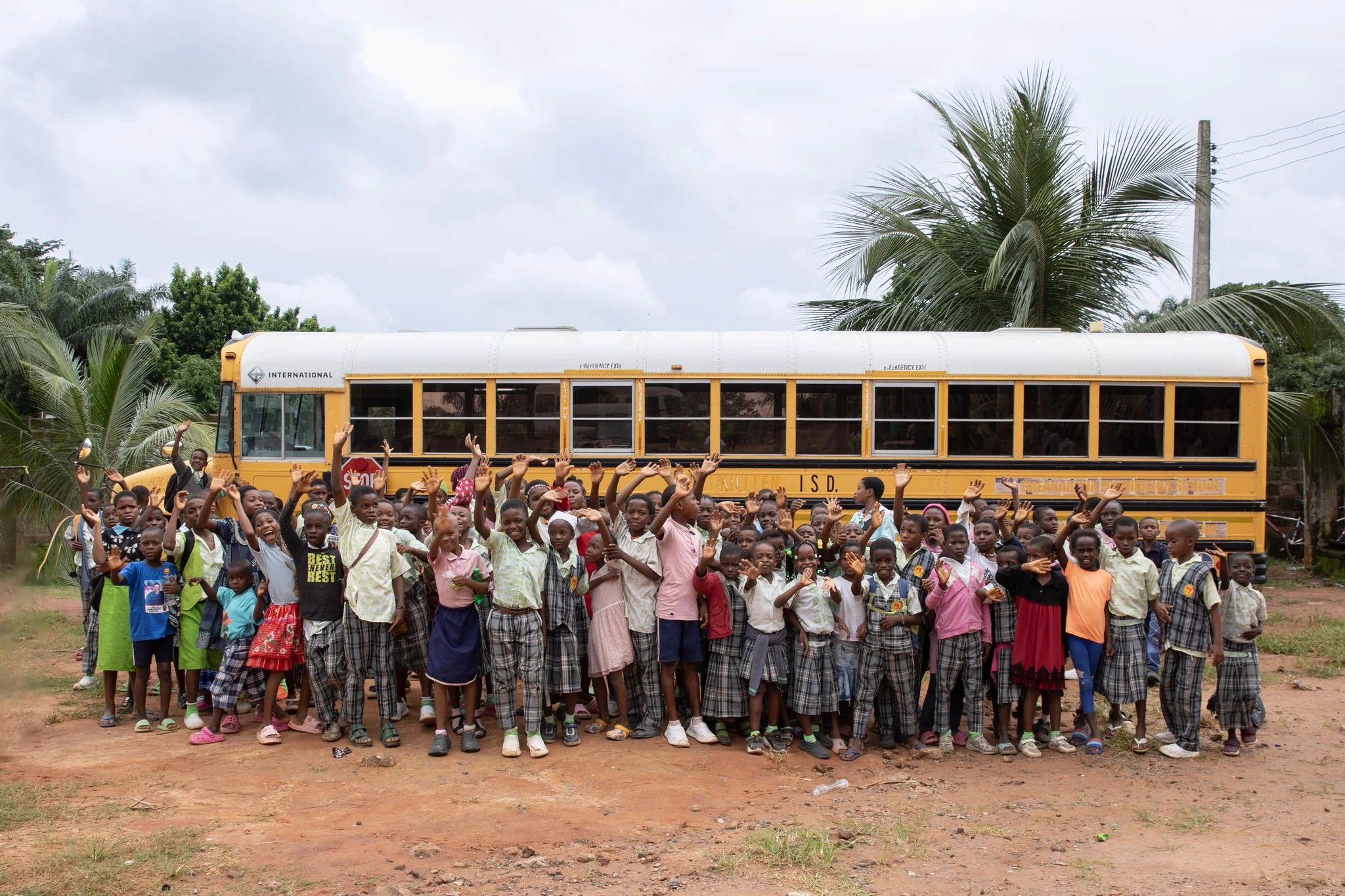 a schoolbus in africa with many waving and smiling kids in front of it