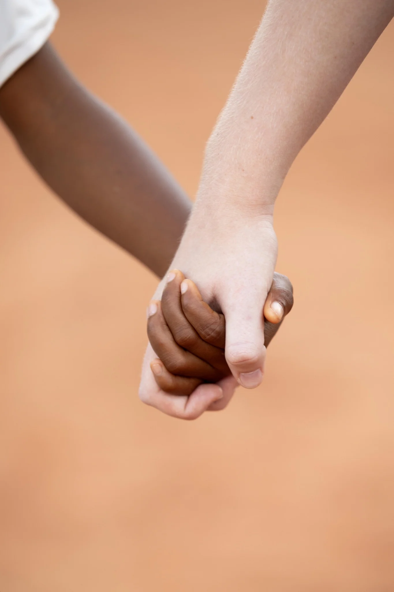 two child hands holding each other, one black, one white